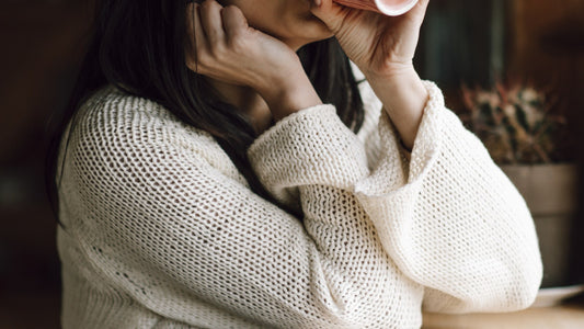 A person in a cozy sweater holding a warm mug with both hands at a wooden table