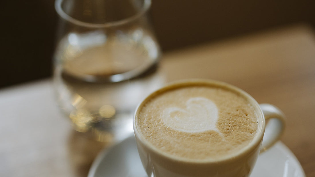 A clear glass of water on a wooden table next to a warm cup of coffee, no people