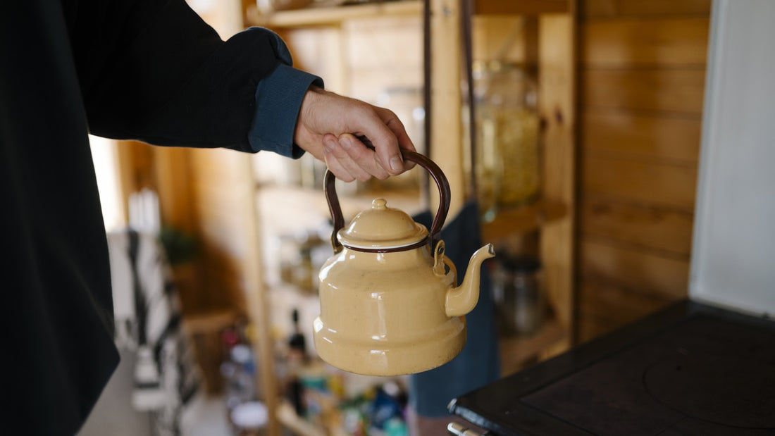 Hand holding a vintage yellow tea kettle in a warm wooden kitchen