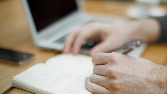Person writing a short list in a notebook at a wooden desk