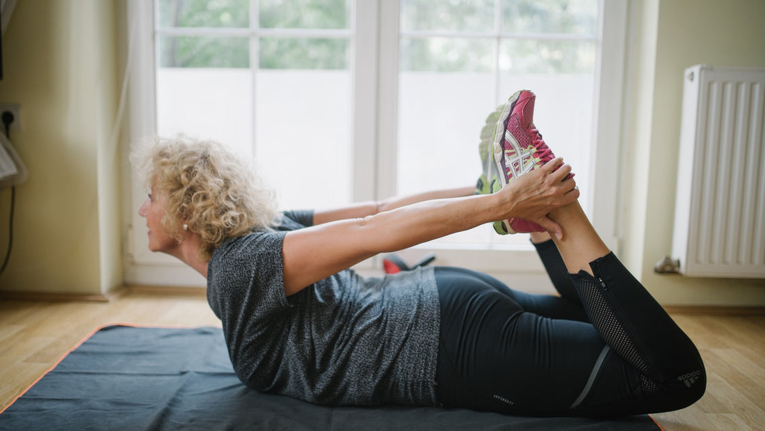 Senior woman practicing a gentle floor stretch on an exercise mat near a sunlit window