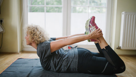 Senior woman practicing a gentle floor stretch on an exercise mat near a sunlit window
