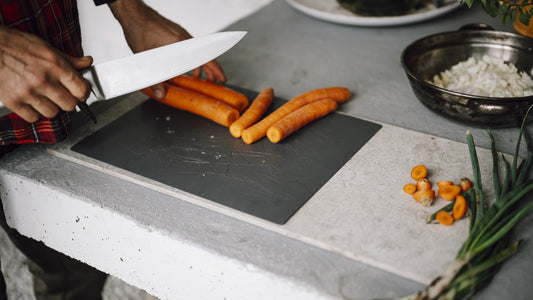 Fresh orange carrots being sliced with a chef knife on a kitchen cutting board