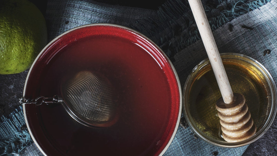Warm cup of freshly steeped herbal tea with a tea strainer and honey on a textured rustic surface