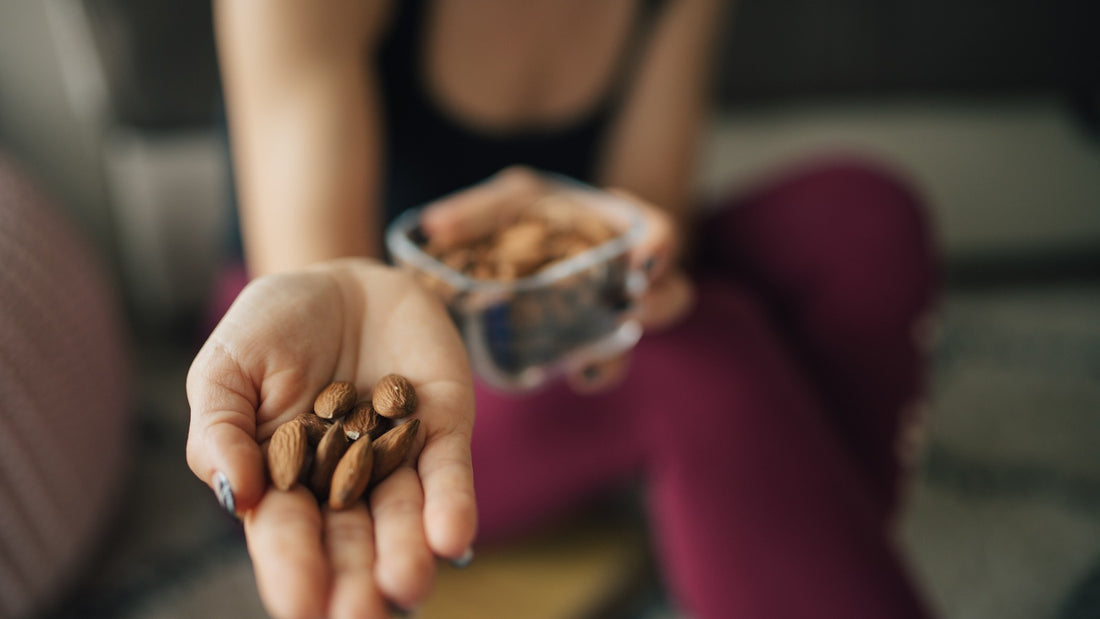 Woman holding almonds in her hand while seated comfortably at home with a snack bowl