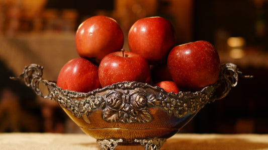 Ornate bowl filled with crisp red apples resting on a dining table