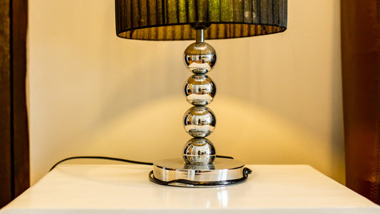 A decorative table lamp on a white nightstand in a bedroom, no phone or people visible