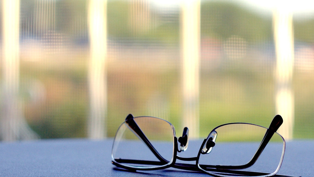 Reading glasses resting on a table near a bright window
