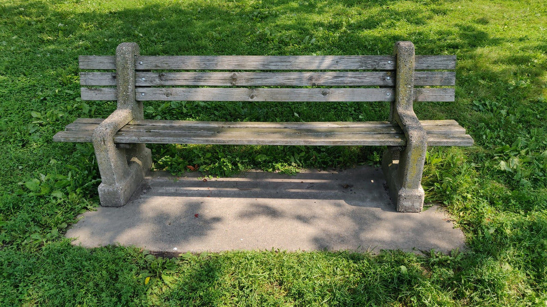 Wooden park bench on a paved pad surrounded by green grass