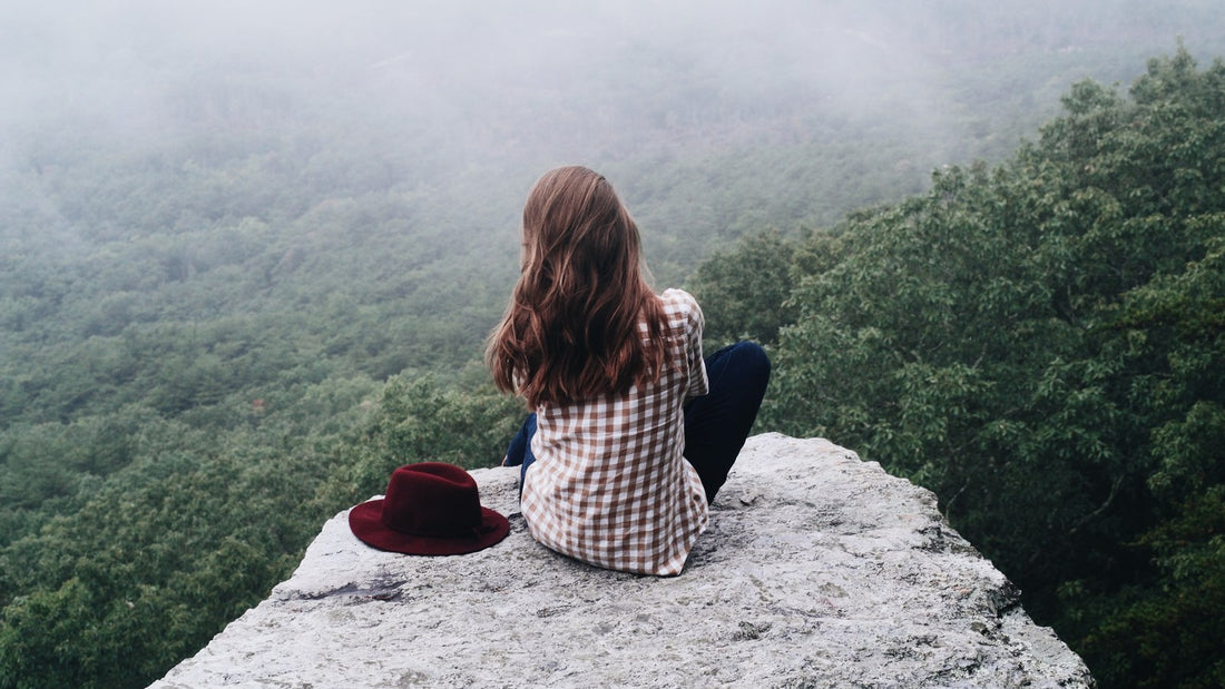 Woman sitting quietly on a rock overlooking a misty green valley