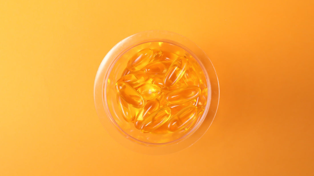 Unlabeled clear bottle filled with golden softgel capsules on an orange background