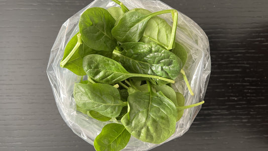 Fresh spinach leaves in a produce bag on a wooden table, no people