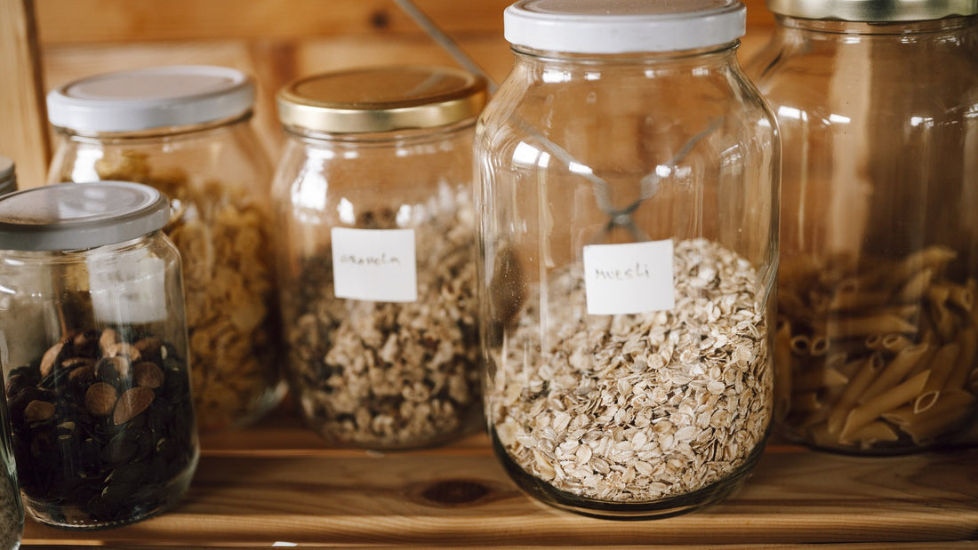 Glass jars of grains, oats, nuts and pasta arranged on a wooden pantry shelf