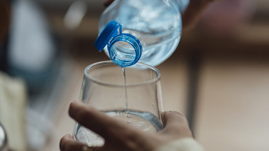 Hands pouring water from a clear bottle into a glass