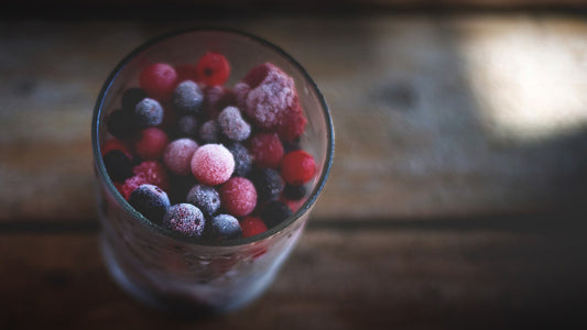 A glass bowl of frosty mixed frozen berries on a wooden table
