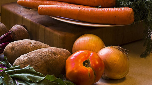 Carrots, beets, potatoes, onions, tomato, and herbs beside a cutting board