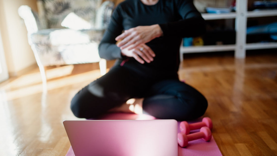 Person seated cross-legged on a mat at home doing a gentle forward stretch