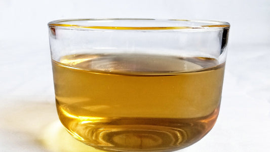 Plain glass cup filled with golden herbal tea on a light background