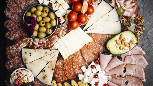 Overhead view of an assorted lunch board with sliced foods, cheeses, vegetables, olives, nuts, and crackers