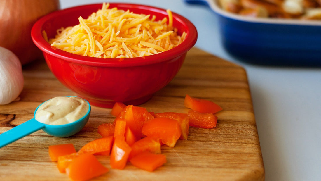 Chopped orange bell pepper on a wooden board beside shredded cheese and a spoon of dressing