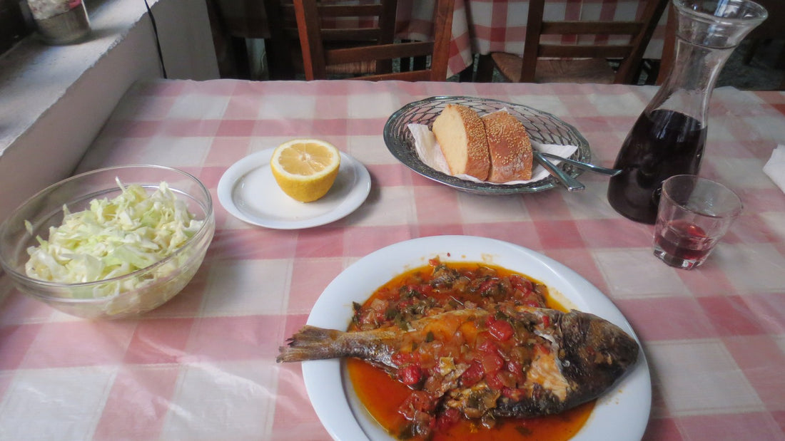 A cooked fish dish with tomato sauce, bread, salad, and lemon on a restaurant table
