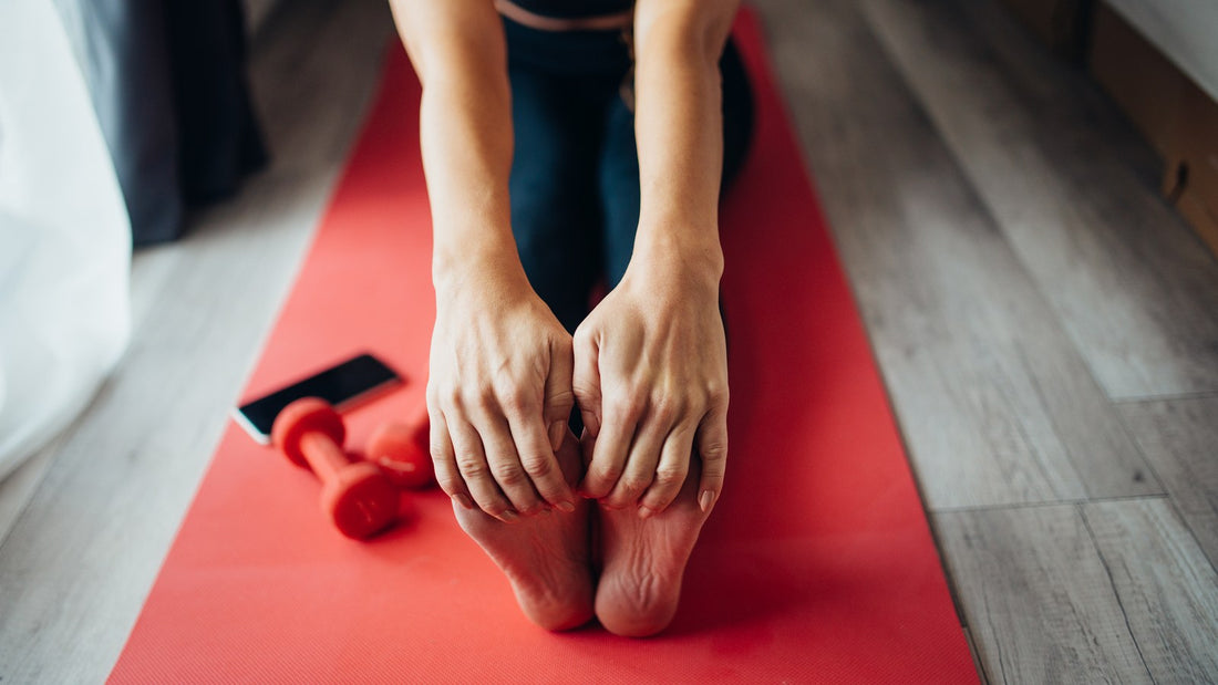 Close-up of a person seated on a red mat holding their feet during a gentle stretch at home