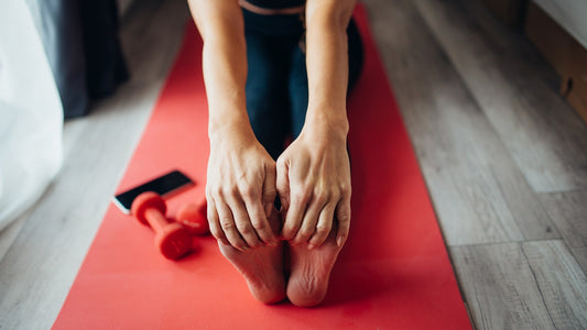 Close-up of a person seated on a red mat holding their feet during a gentle stretch at home