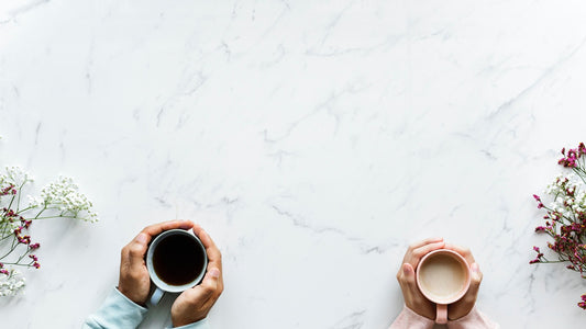 Two people holding warm drinks over a pale table with small flowers at the edges