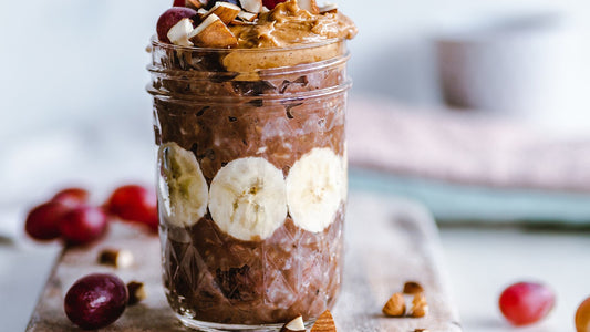 Jar of chocolate oatmeal topped with banana, grapes, nut butter, and chopped nuts