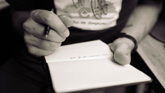 Person writing a short note in an open notebook at a wooden table