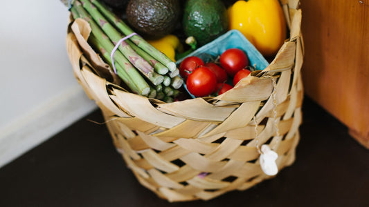 Basket filled with asparagus, tomatoes, avocados and yellow bell peppers