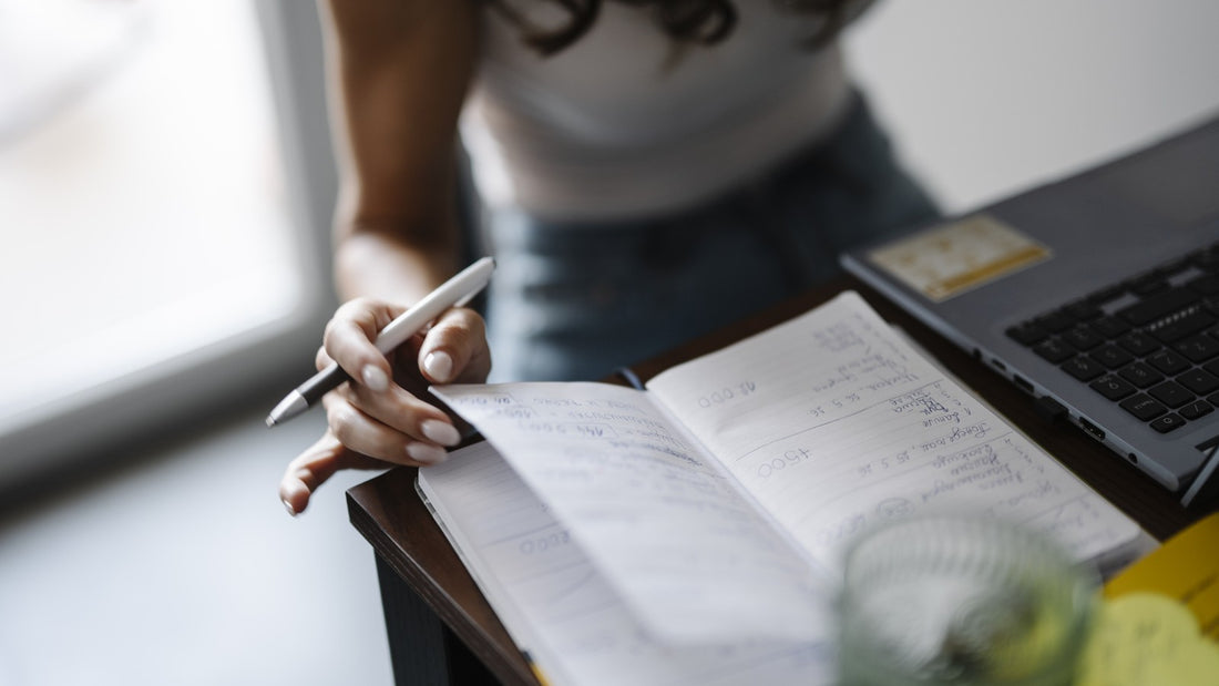 Person writing a short note in an open notebook at a desk