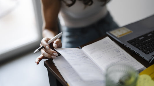 Person writing a short note in an open notebook at a desk