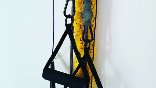 Yellow resistance tubes and black exercise handles hanging against a white wall