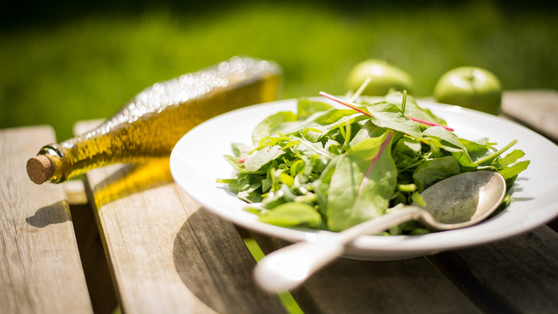 Fresh green salad on a white plate with a bottle of olive oil and green apples on a wooden table