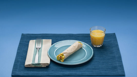 Whole grain wrap and orange juice on a blue table for a fiber-friendly meal article