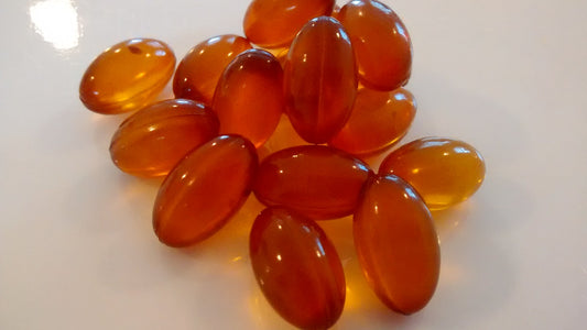 Unbranded amber supplement softgels on a plain white surface