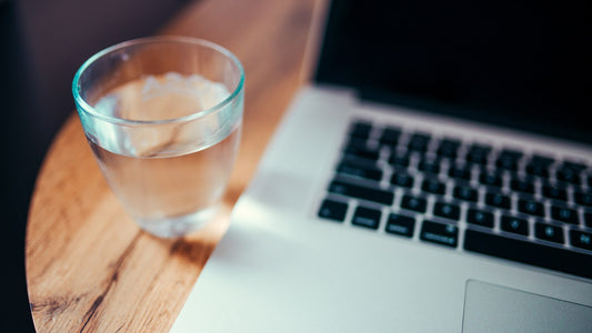 A clear glass of water beside a laptop on a wooden table