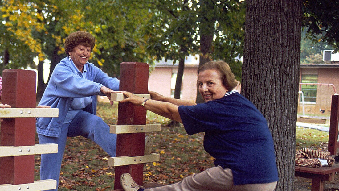 Two older women using an outdoor rail for a short movement pause