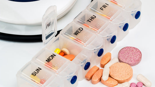 Weekly organizer with assorted supplement capsules and tablets on a white surface