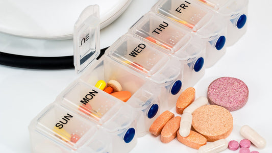 Weekly organizer with assorted supplement capsules on a white surface