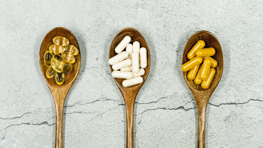Three wooden spoons holding golden, white, and yellow supplement capsules on a gray stone surface