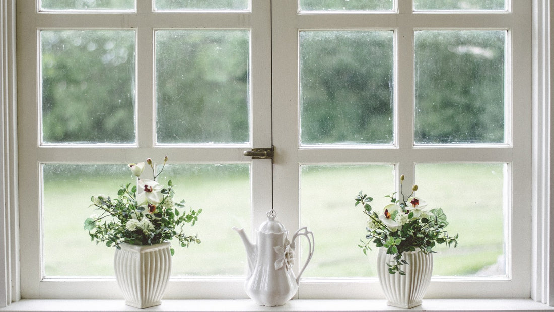 White teapot on a windowsill between two small flower arrangements