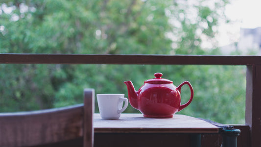 Red teapot and white ceramic mug resting on an outdoor wooden table overlooking trees