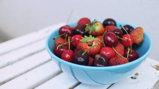 Turquoise bowl filled with strawberries and cherries on a white table