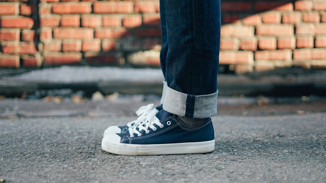 Person wearing laced navy walking shoes beside a brick wall