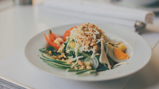 A colorful salad with greens, cucumber, tomato, egg, and a crunchy topping