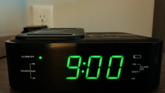 Black digital alarm clock showing nine o'clock on a bedside table