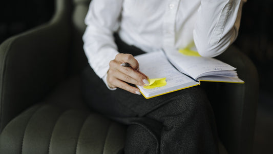Person writing in an open notebook while seated in a dark armchair