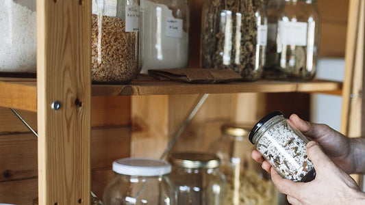 Jars of pantry ingredients on a wooden kitchen shelf.
